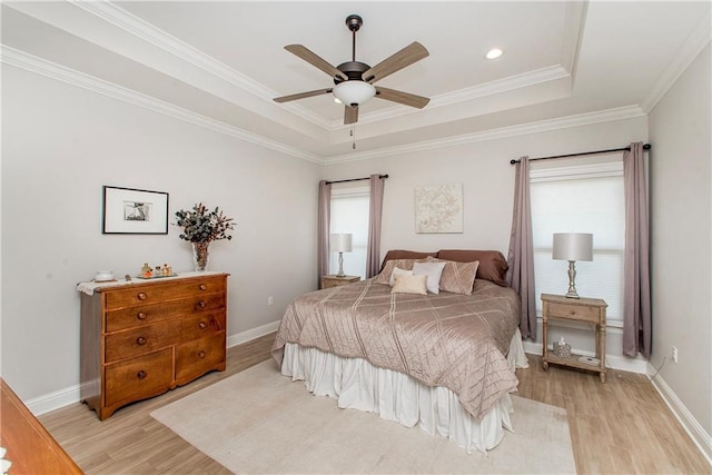 bedroom featuring light wood-style floors, multiple windows, and a tray ceiling