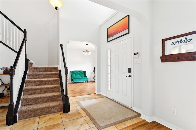 tiled foyer entrance with a chandelier, stairs, arched walkways, and baseboards
