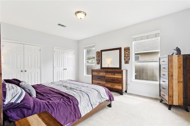 bedroom featuring baseboards, light colored carpet, visible vents, and two closets