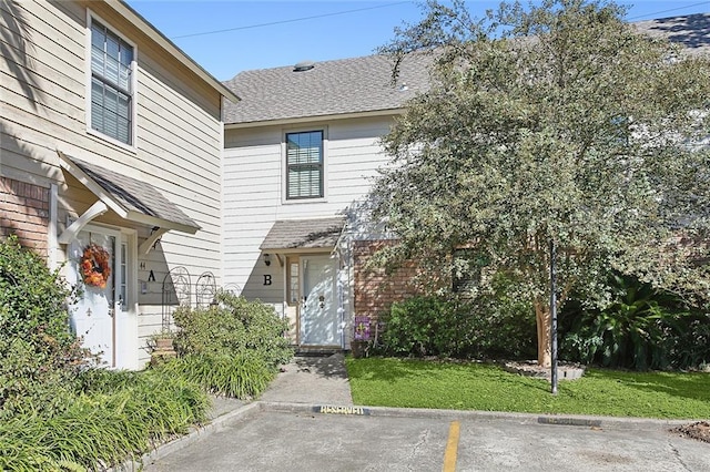 view of front of home with brick siding, uncovered parking, roof with shingles, and a front lawn