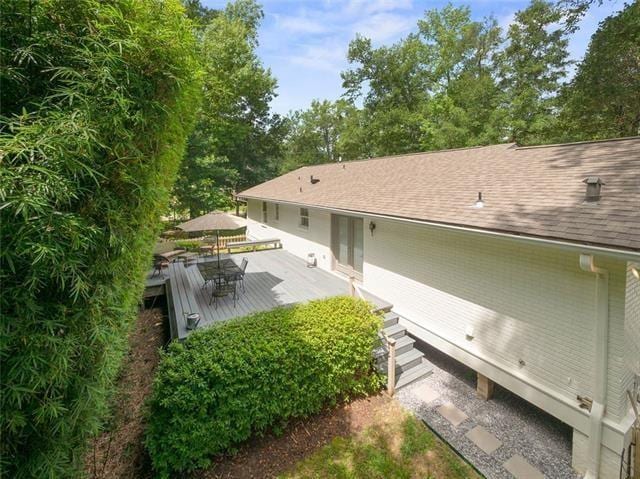 back of house featuring roof with shingles and a wooden deck