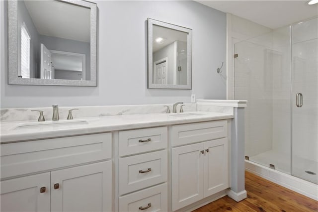 full bathroom featuring double vanity, wood finished floors, a stall shower, and a sink