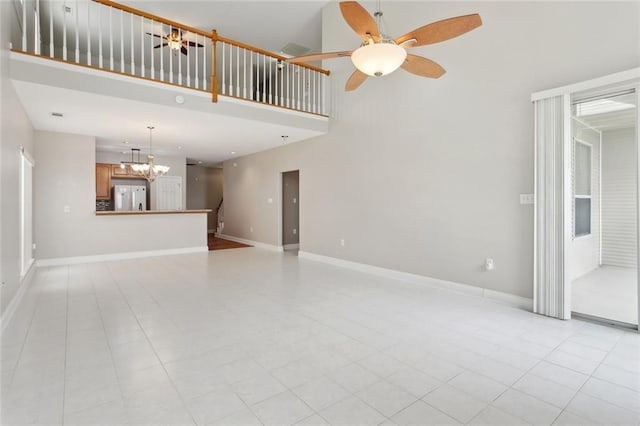 unfurnished living room with light tile patterned flooring, a high ceiling, ceiling fan with notable chandelier, and baseboards
