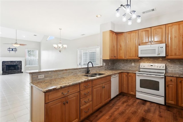 kitchen featuring a sink, a peninsula, white appliances, light stone counters, and visible vents