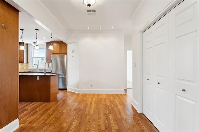 5512 S Tonti St, New Orleans, LA 70125 - kitchen with tasteful backsplash, brown cabinets, freestanding refrigerator, visible vents, and light wood-style flooring