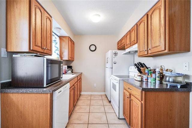 kitchen with under cabinet range hood, brown cabinetry, light tile patterned floors, white appliances, and dark countertops