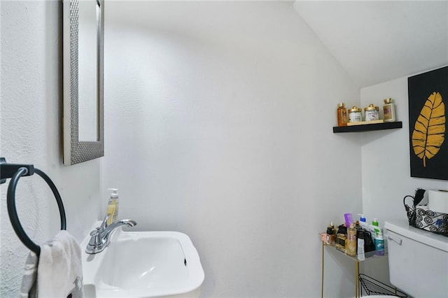 half bathroom with vaulted ceiling, toilet, and a sink