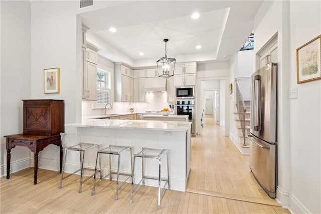 kitchen featuring appliances with stainless steel finishes, a peninsula, light wood finished floors, a sink, and a breakfast bar