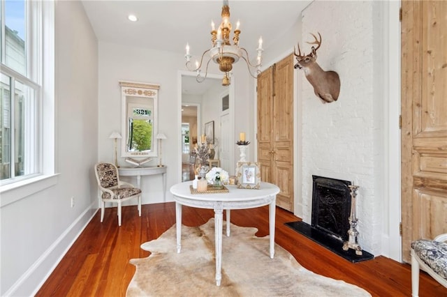 living area with an inviting chandelier, a fireplace with raised hearth, and wood finished floors