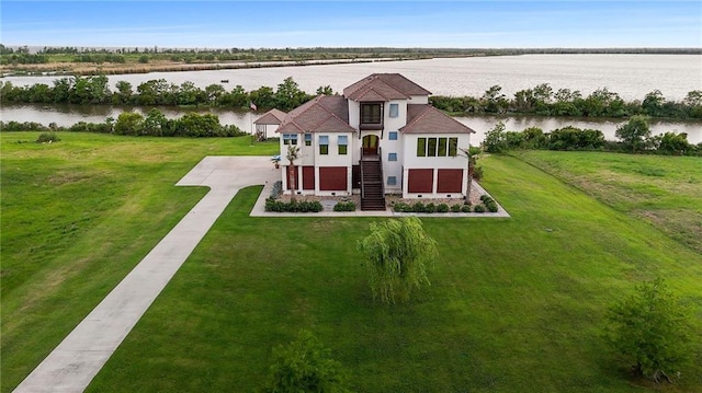 view of front of property with concrete driveway, stucco siding, stairway, a front lawn, and a water view