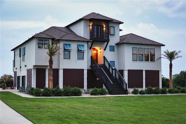 view of front of home featuring an attached garage, stucco siding, a front lawn, and a balcony