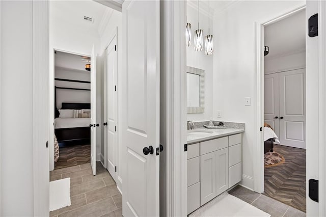 ensuite bathroom with connected bathroom, visible vents, vanity, and ornamental molding