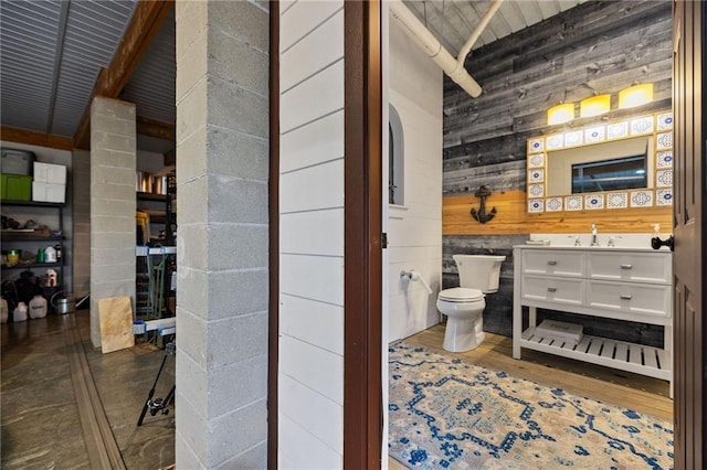 bathroom featuring toilet, wood walls, vanity, and wood finished floors