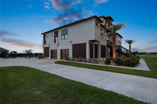 view of home's exterior featuring an attached garage, stucco siding, concrete driveway, stairway, and a yard