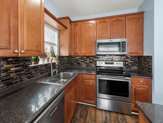 1001 W Chateau Lafitte Dr, Kenner, LA 70065 - kitchen featuring appliances with stainless steel finishes, a sink, dark wood-style floors, brown cabinetry, and a textured ceiling