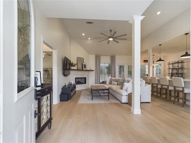 living room featuring light wood finished floors, a fireplace, ceiling fan, and ornate columns