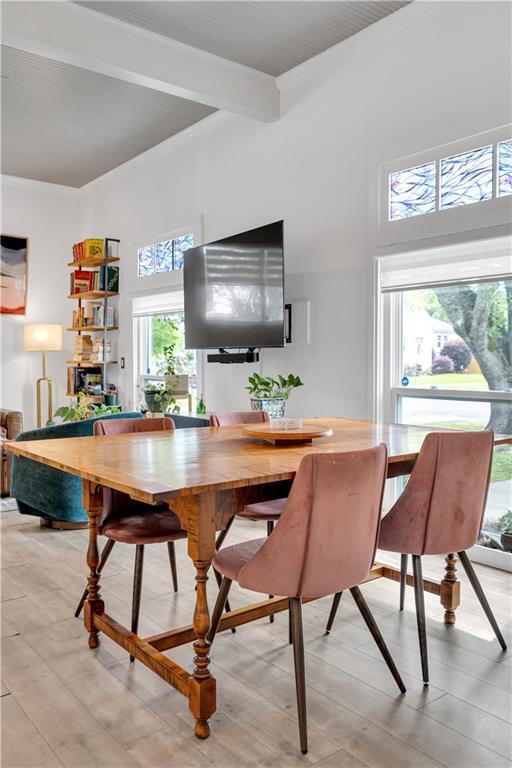 dining room featuring a high ceiling, light wood-style flooring, and beamed ceiling