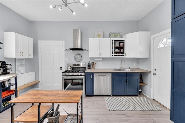 kitchen featuring wall chimney range hood, stainless steel appliances, a sink, blue cabinets, and white cabinets