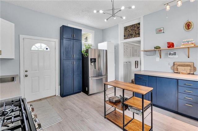 kitchen featuring stainless steel fridge, blue cabinets, open shelves, light wood-style floors, and healthy amount of natural light