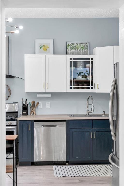 kitchen with stainless steel appliances, a sink, blue cabinets, white cabinets, and light countertops