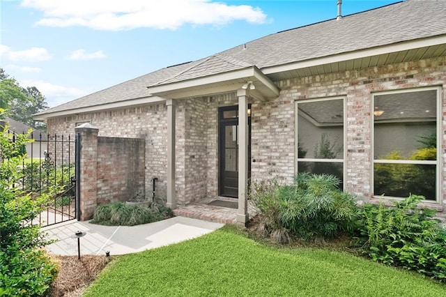 property entrance with a yard, roof with shingles, brick siding, and a gate