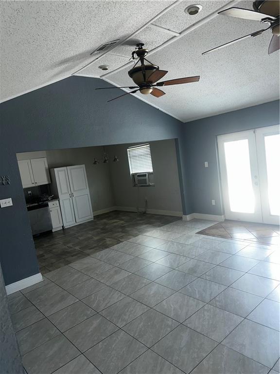 unfurnished living room with lofted ceiling, a textured ceiling, dark tile patterned floors, a ceiling fan, and baseboards