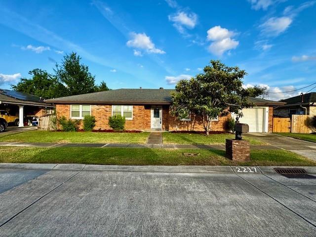ranch-style house featuring concrete driveway, a front yard, an attached garage, and fence