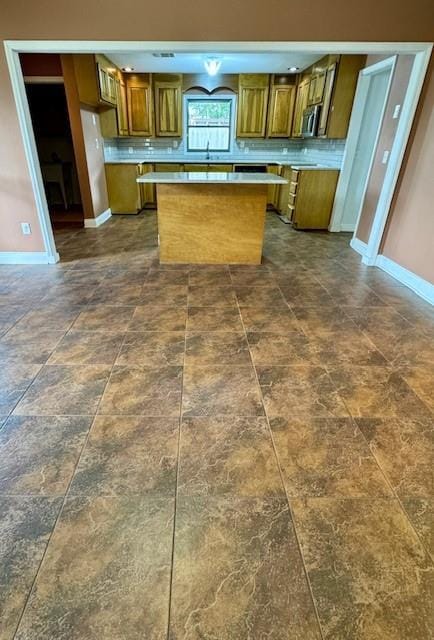 kitchen with a center island, brown cabinets, stainless steel microwave, baseboards, and light countertops