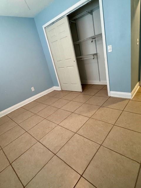 unfurnished bedroom featuring light tile patterned floors, baseboards, and a closet
