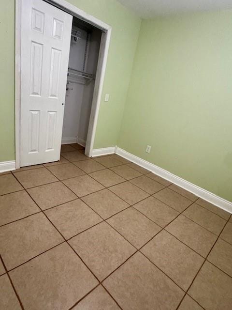 unfurnished bedroom featuring light tile patterned floors, baseboards, and a closet