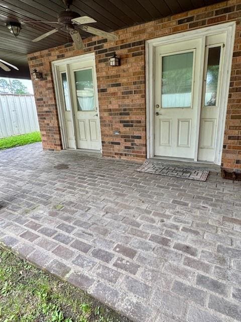 doorway to property featuring a patio area, a ceiling fan, and brick siding
