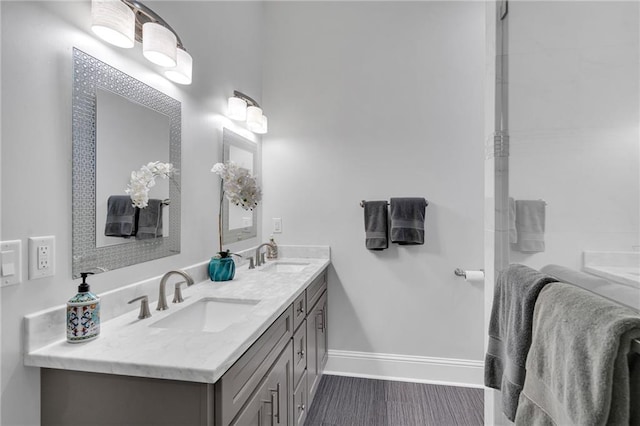 full bath featuring baseboards, double vanity, and a sink