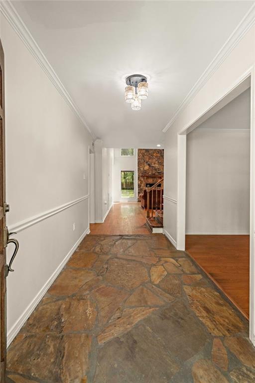 hallway with stone floors, crown molding, baseboards, and a chandelier