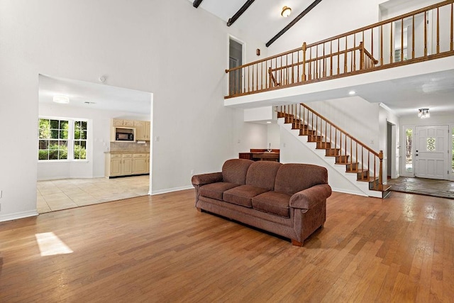living area featuring baseboards, stairway, light wood finished floors, and high vaulted ceiling
