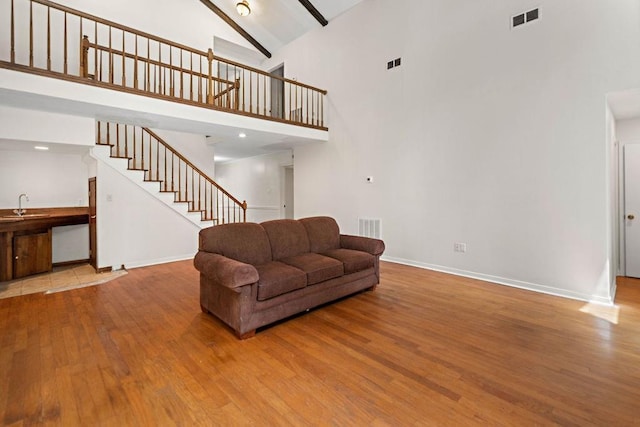 living area featuring wood finished floors, high vaulted ceiling, visible vents, baseboards, and stairs
