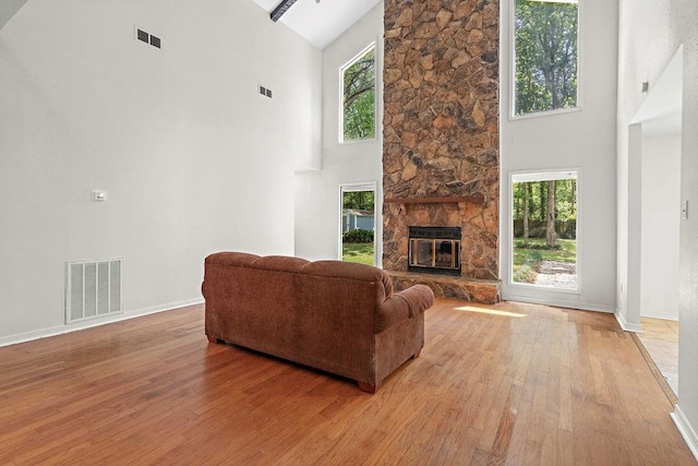 living area with a fireplace, light wood-style flooring, high vaulted ceiling, and visible vents