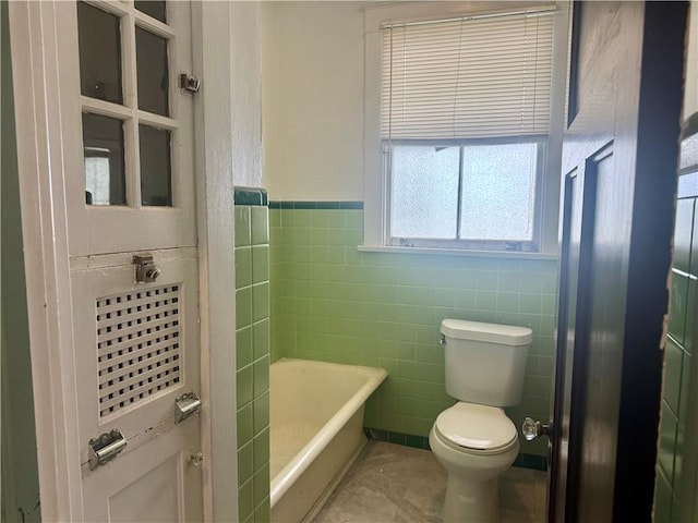 bathroom with toilet, a bath, tile walls, and a wainscoted wall