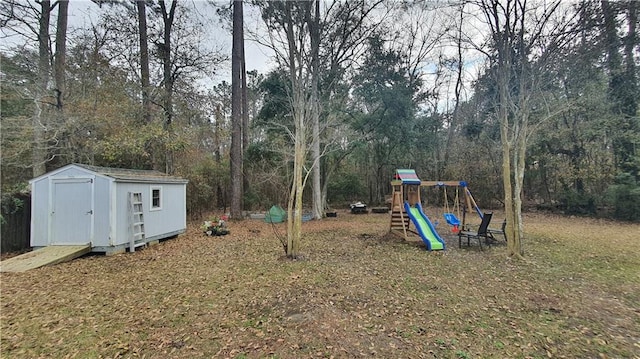 view of yard featuring a playground, a storage unit, an outdoor structure, and view of wooded area