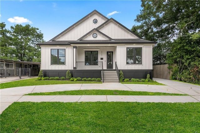 modern farmhouse with a front lawn, board and batten siding, covered porch, and fence
