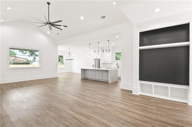 unfurnished living room featuring ceiling fan with notable chandelier, high vaulted ceiling, visible vents, light wood-style floors, and recessed lighting
