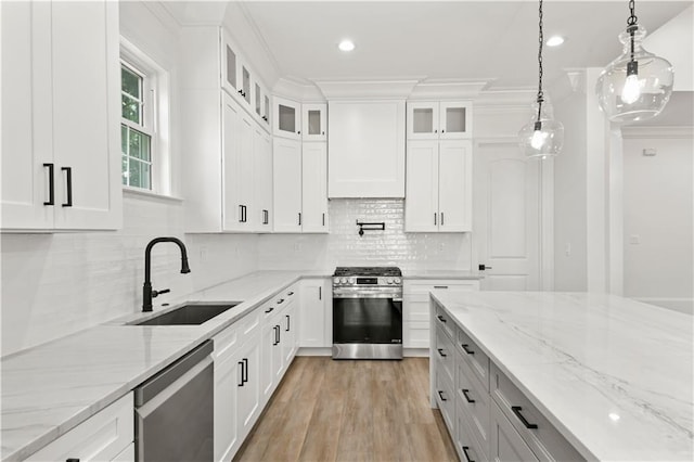 kitchen with hanging light fixtures, glass insert cabinets, a sink, appliances with stainless steel finishes, and light wood-style floors