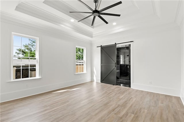 empty room featuring ceiling fan, ornamental molding, a barn door, and wood finished floors