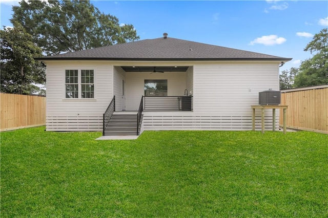 rear view of house featuring a yard, a shingled roof, and a fenced backyard