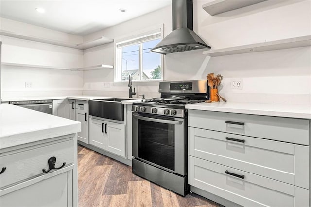 kitchen with a sink, open shelves, wood finished floors, wall chimney range hood, and stainless steel appliances