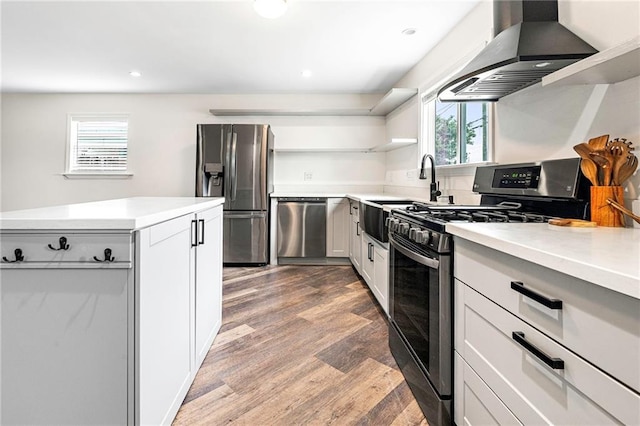 kitchen featuring stainless steel appliances, open shelves, wall chimney range hood, and a healthy amount of sunlight