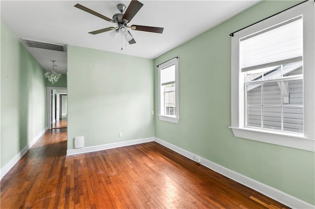 unfurnished room featuring baseboards, hardwood / wood-style floors, visible vents, and ceiling fan with notable chandelier