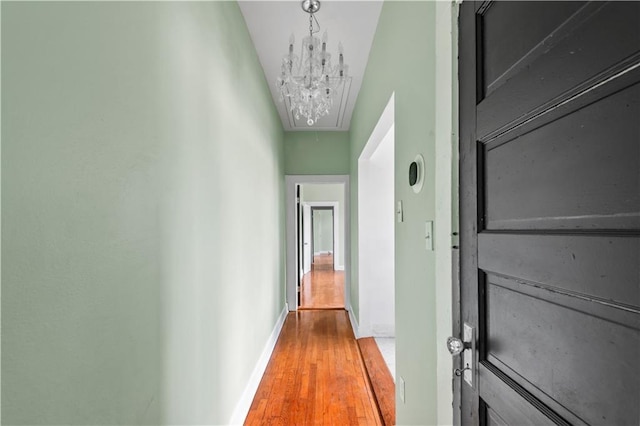 hallway with baseboards, an inviting chandelier, attic access, and wood finished floors