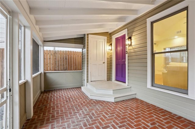 unfurnished sunroom with wooden walls, brick floor, and beamed ceiling