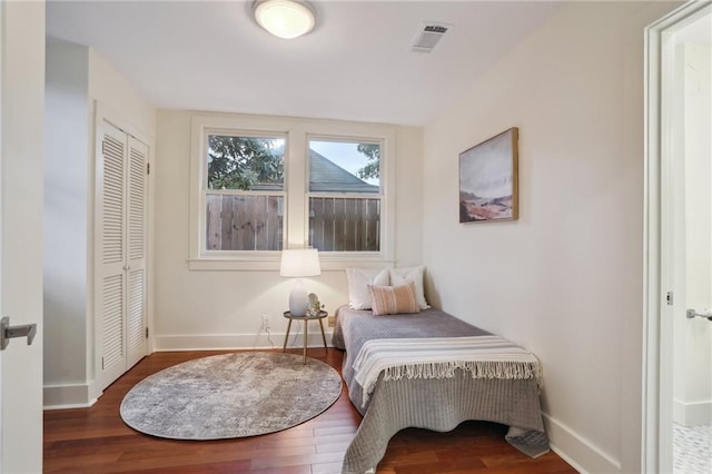 bedroom with a closet, visible vents, wood finished floors, and baseboards