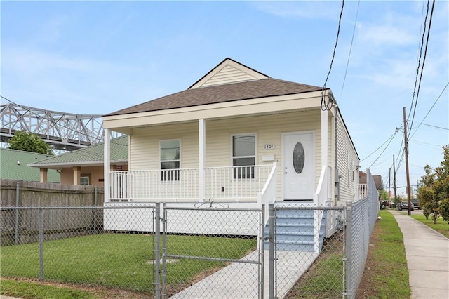 shotgun-style home featuring covered porch, a gate, a shingled roof, a front yard, and a fenced front yard